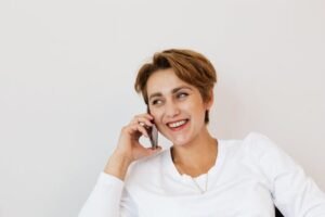 A smiling woman with short hair talking on a phone, seated indoors.
