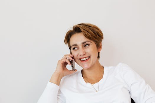 A smiling woman with short hair talking on a phone, seated indoors.
